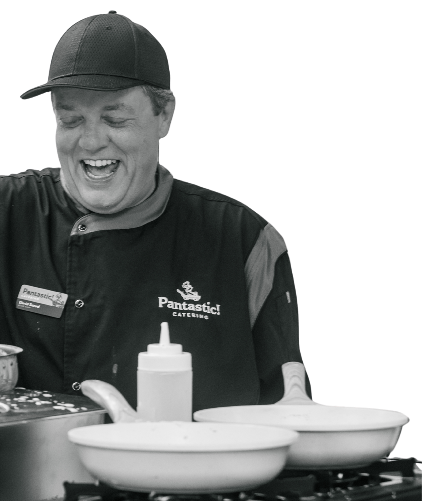 A candid black-and-white photo of Chef David Sneed laughing while preparing fresh meals at a live event.