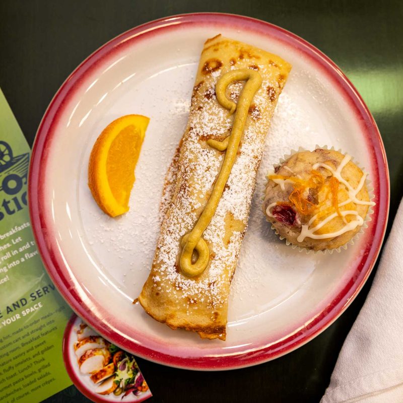A savory breakfast crepe served on a real ceramic plate with fresh fruit and a side dish.