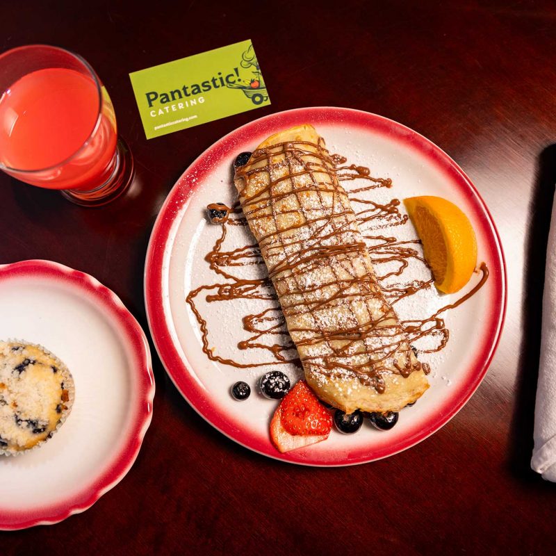 A chocolate-drizzled sweet crepe paired with a fresh fruit juice and a side cookie on real tableware.