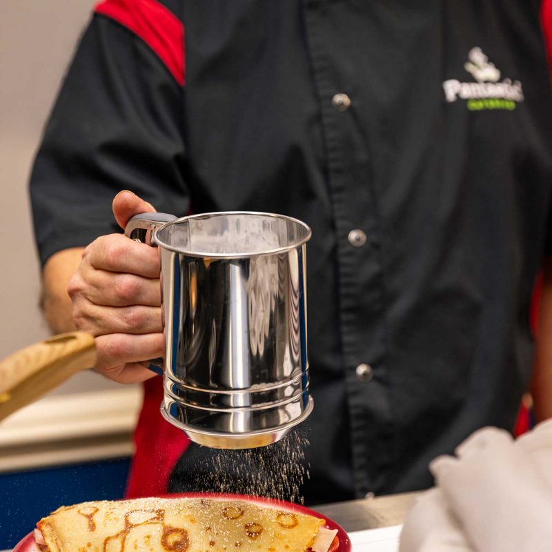 Chef David Sneed sifting powdered sugar over a fresh, golden crepe during a live catering event.